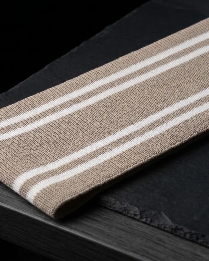 Pieza tejida beige con franjas blancas sobre una superficie oscura